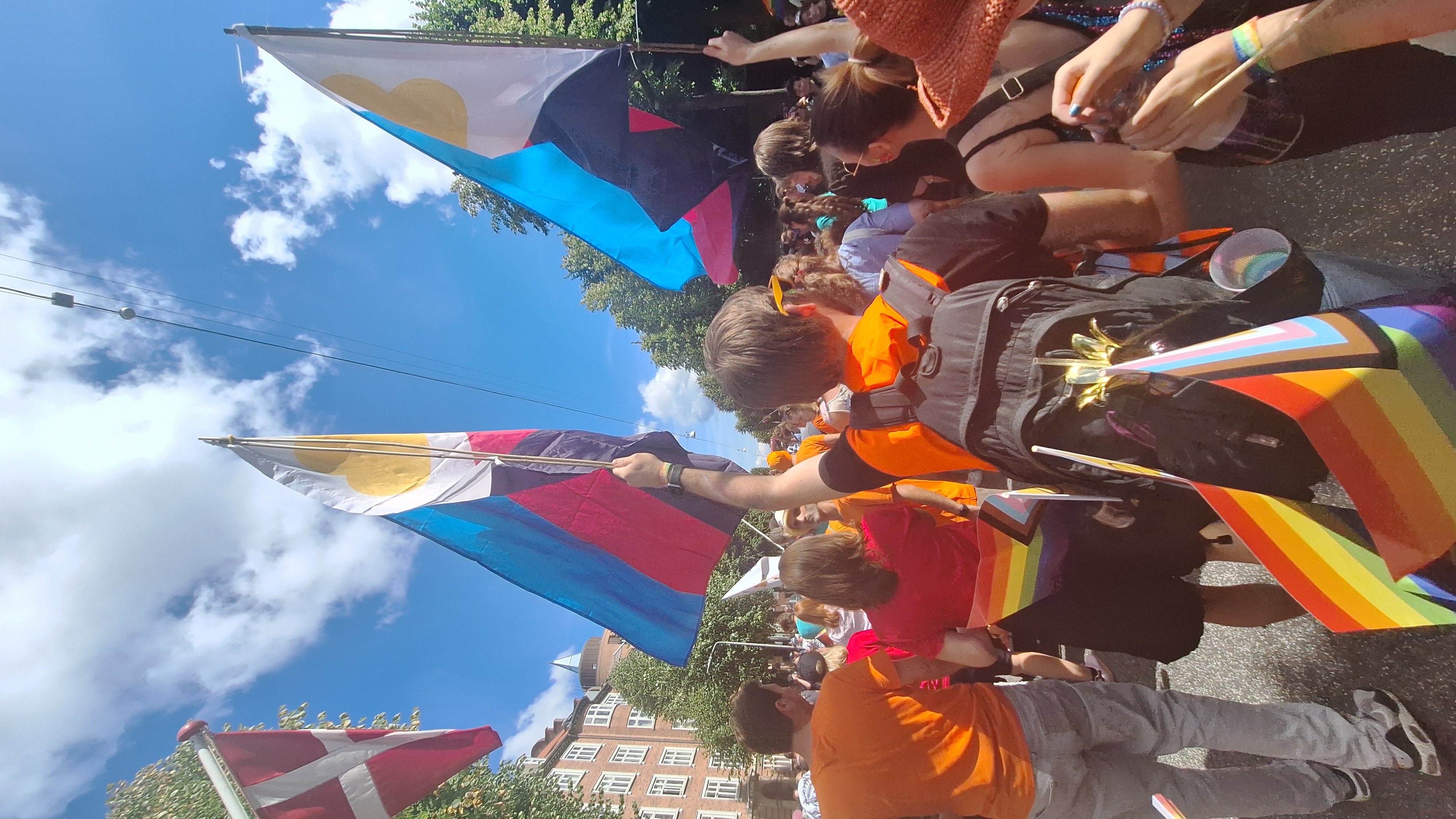 To personer går arm i arm og vifter med polyamori-flag ved Pride
